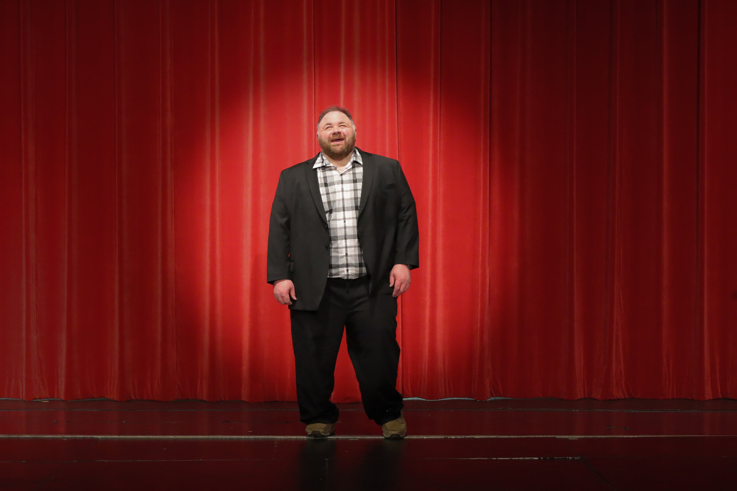 Kevin Lowe standing center stage before red theater curtains